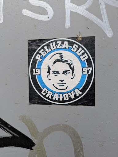 The sticker features a black and white portrait of a man inside a blue and white circle. The text 'PELUZA-SUD' and 'CRAIOVA' are printed in bold letters around the circle, with the years '19' and '97' flanking the portrait.