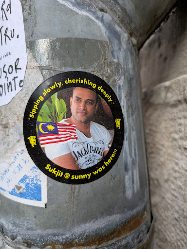 The sticker shows a man in a white Jack Daniel's t-shirt with the Malaysian flag. The text "sipping slowly, cherishing deeply" arches above him, and the text "Sukjit @ sunny was here!!!" appears below the image.