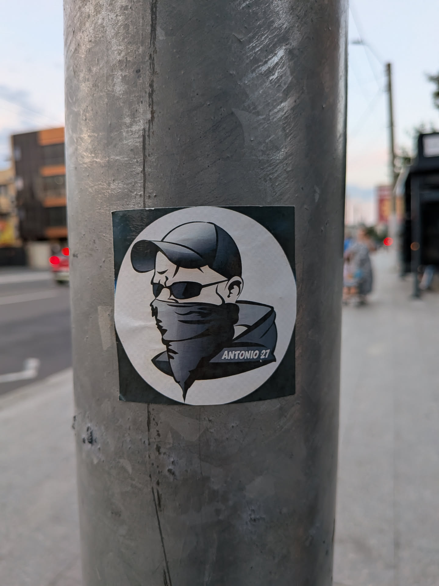 Square sticker with a circular grayscale graphic of a man wearing a cap, sunglasses, and a face bandana. The text 'ANTONIO 21' is on his collar.