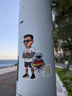 Street sticker Die-cut sticker depicting a cartoon tattooed man in sunglasses next to a sacred heart emblem. Includes a QR code and Instagram handle.
