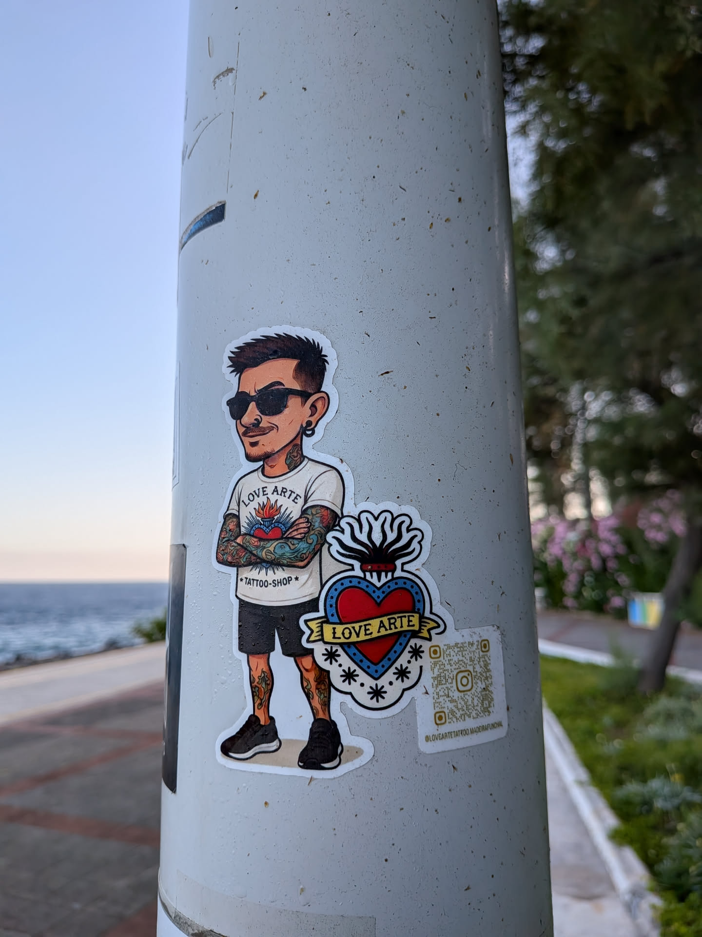 Die-cut sticker depicting a cartoon tattooed man in sunglasses next to a sacred heart emblem. Includes a QR code and Instagram handle.