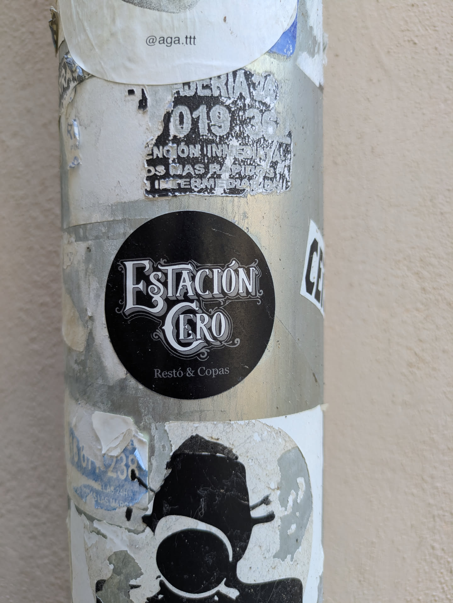 The sticker features the name Estación Cero in a decorative font, with the tagline Restó & Copas underneath, indicating it is a restaurant and bar. The sticker is on a metal pole, surrounded by other stickers.