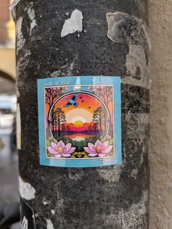 The sticker showcases a picturesque sunset over a lake, reflected in the water with silhouettes of trees lining the horizon. A blue bird soars through the sky above the setting sun. Two large pink lotus flowers sit at the bottom of the design, with the text "MAGNOLIAN MOODS" at the top and "SUNBEAMS" at the bottom.