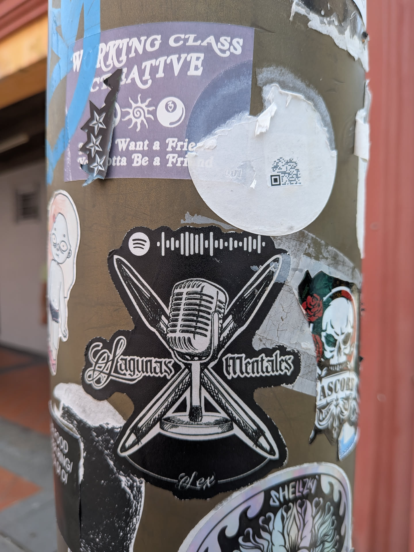 A die-cut black sticker featuring a white illustration of a vintage microphone over crossed pens. It displays the text 'Lagunas Mentales' in gothic script, 'Alex' at the bottom, and a Spotify logo with a scannable code at the top.