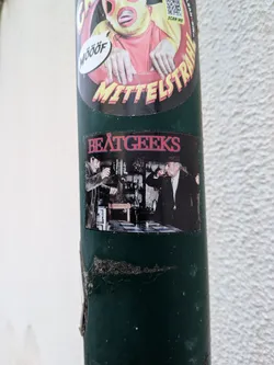 Street sticker A rectangular sticker with the red text 'BEATGEEKS' at the top. Below is a black-and-white photo of two older men in hats drinking in a rustic room.