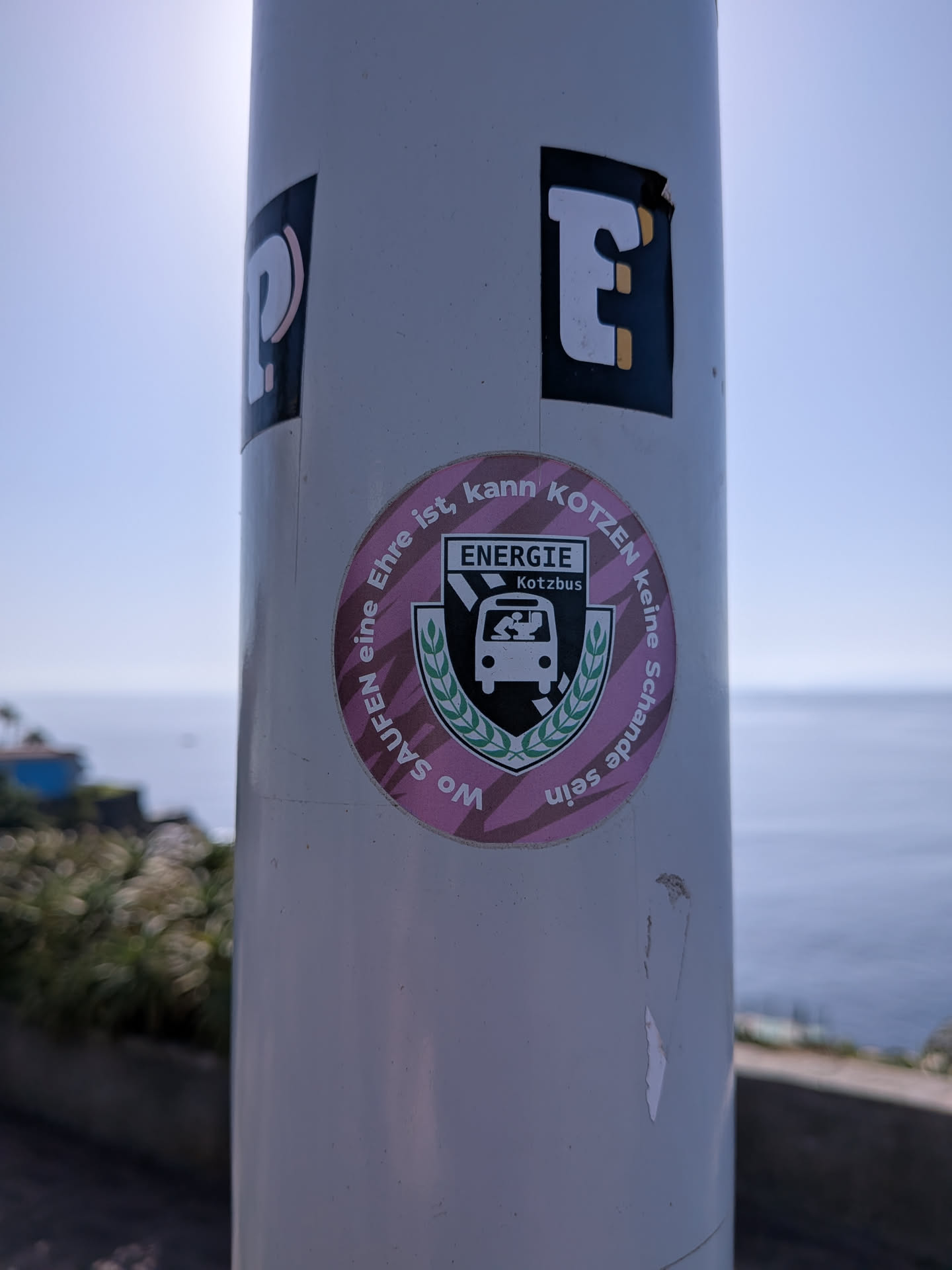 A round pink sticker featuring a parody crest of FC Energie Cottbus, renamed 'ENERGIE Kotzbus'. The crest depicts a person vomiting from a bus, surrounded by circular German text.