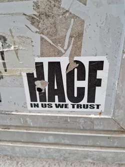 A sticker with the acronym HACF and the text "In us we trust". The sticker is slightly damaged.