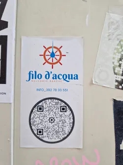 A sticker advertising boat rentals from Filo d'acqua.  The sticker features a logo with a water droplet and a ship's wheel, contact information, and a QR code.