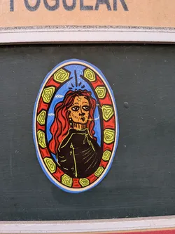 Street sticker An oval sticker depicting a stylized portrait of a person with long red hair and a star on their forehead, smoking a cigarette. The figure is set against a blue sky background and framed by a red border decorated with green spiral patterns.