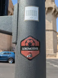 Street sticker The sticker is in the shape of a shield, featuring a soccer ball at the top, the word "LOKOMOTIVE" in bold white letters across the middle, and "LITTENWEILER" in smaller white letters beneath. An illustration of a steam train is at the bottom.