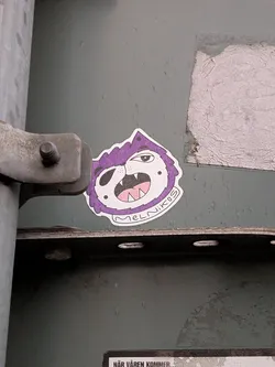 Street sticker The sticker features a cartoonish monster's head with a purple, spiky mane. The monster has a white face with a black eyepatch covering its left eye. Its right eye is open and looking forward. It has a wide-open mouth revealing sharp white teeth and a pink tongue. The outline of the sticker is irregular, following the shape of the monster's head and mane. Below the mouth, in a white arc, is the text 'MELNIKOS'. The sticker has a white border.