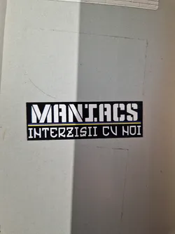 Street sticker A black and white sticker with the words "MANIACS" in a large, bold font on top, and "INTERZISII CU HOI" in a smaller font underneath. The sticker has a simple design and appears to be placed on a light gray surface.