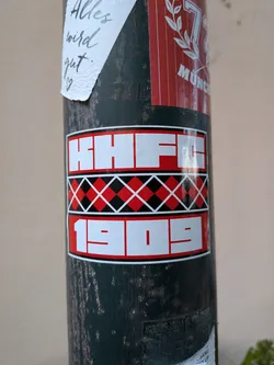 Street sticker Rectangular sticker with three horizontal bands. Top and bottom bands feature bold white text 'HHFC' and '1909' on red backgrounds. The middle band displays a red and black argyle diamond pattern.