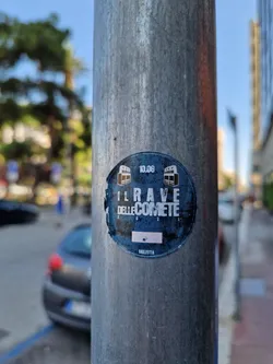 Street sticker A sticker featuring the text "Il Rave delle Comete" (The Comet Rave) and the date 10.06.  The design is round and dark blue with white text and small images. It's affixed to a metal pole.