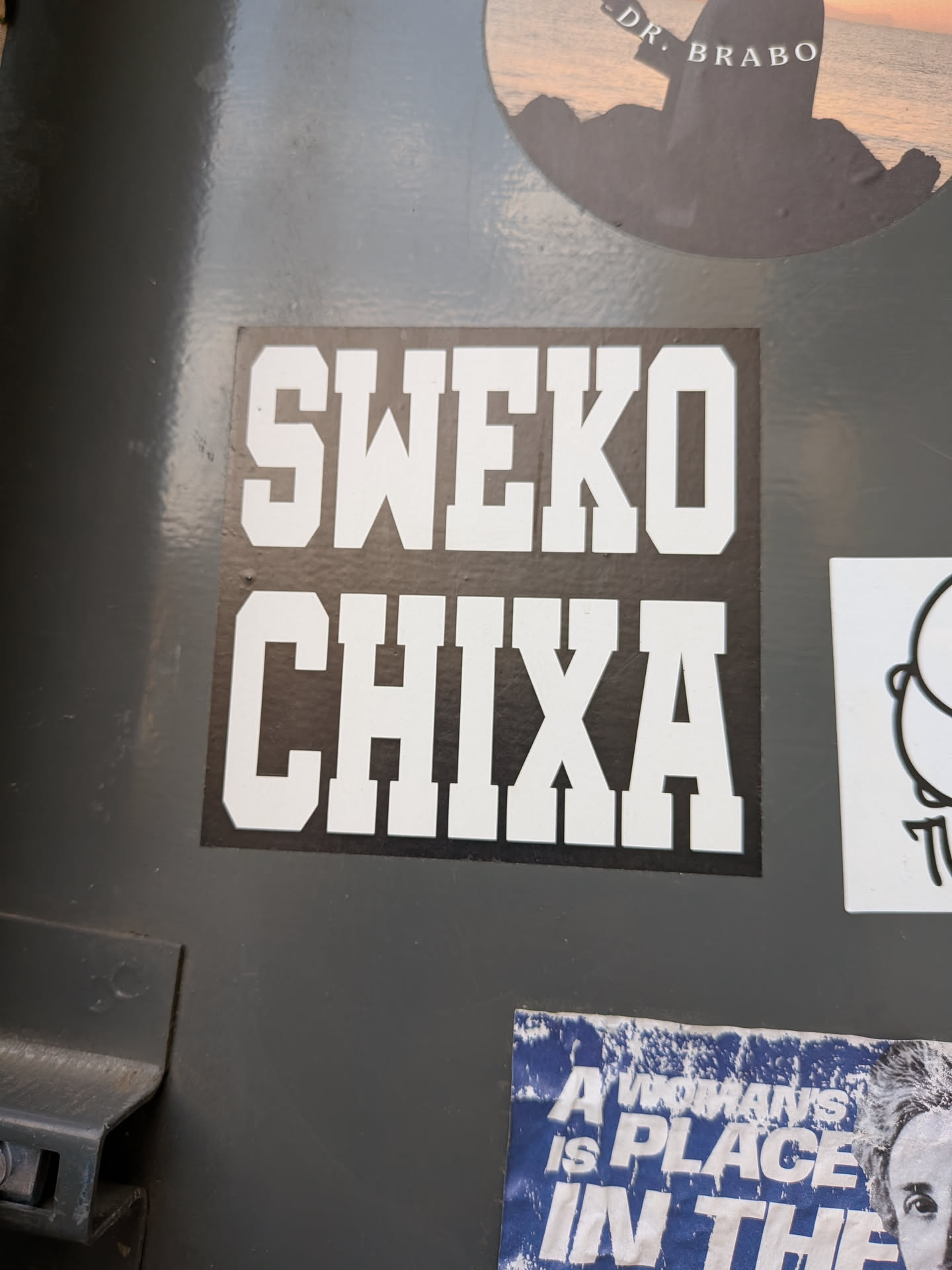 A square black sticker featuring bold, white, collegiate-style block letters spelling 'SWEKO' on the top line and 'CHIXA' on the bottom.