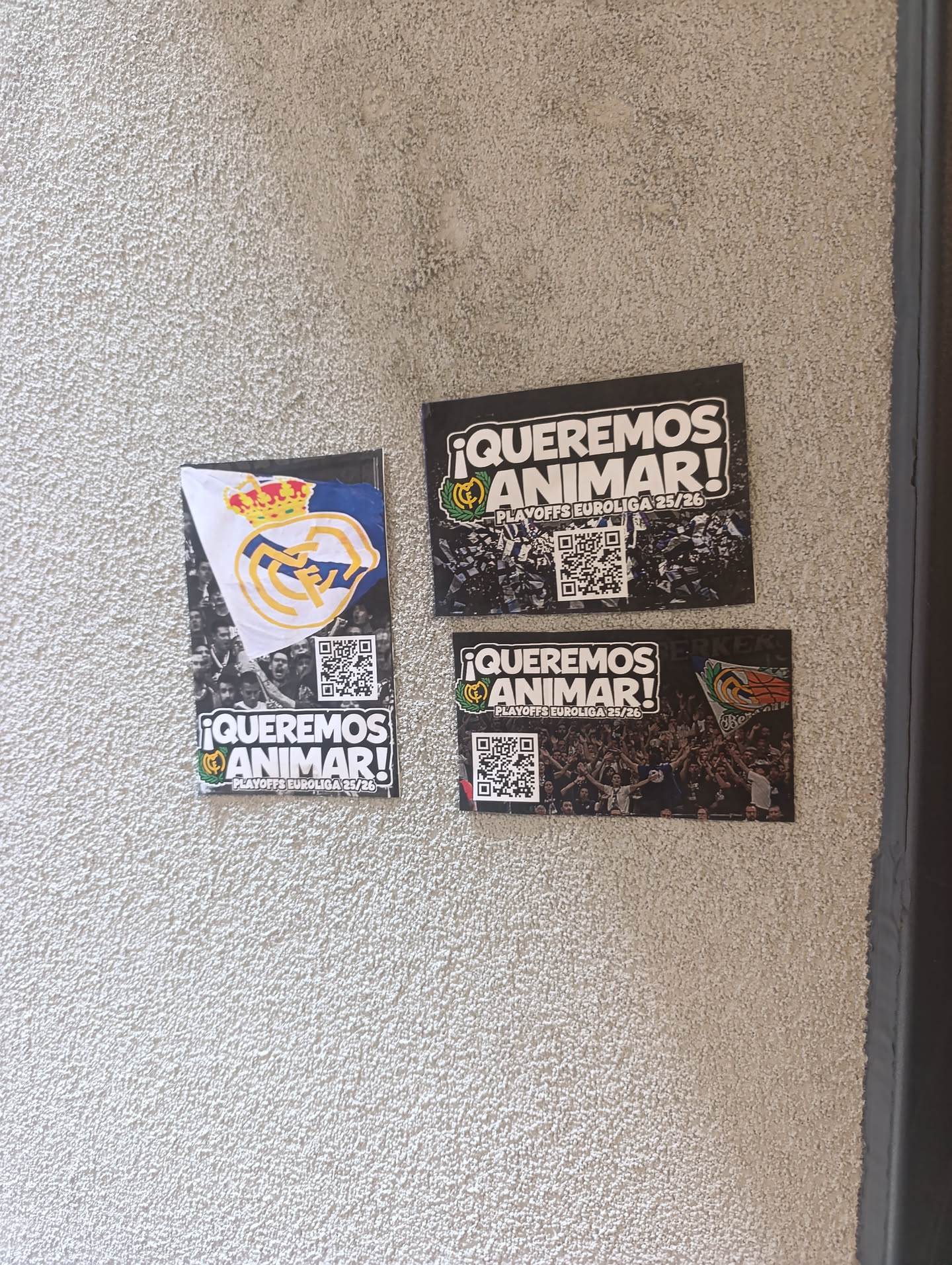 A horizontally oriented rectangular sticker with a dark, abstract background resembling shattered glass or a digital effect. The top section features bold white text '¡QUEREMOS ANIMAR!' (We Want to Cheer!) with a green outline, and below it, 'PLAYOFFS EUROLIGA 23/26' in smaller white text. A small Real Madrid crest, featuring a crown and the 'RM' monogram, is visible to the left of the main text. In the bottom center, a black and white QR code is prominently displayed against the dark background.