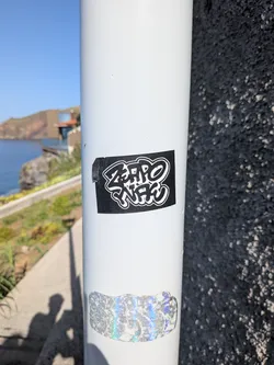 Street sticker A rectangular black sticker with stylized white graffiti lettering reading 'ZERO WAC' outlined in white, affixed to a white metal pole.
