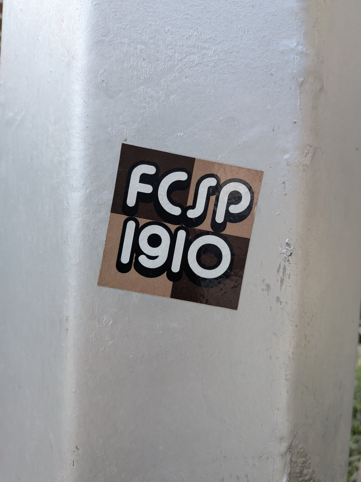 A square sticker featuring a brown and tan checkerboard pattern. The text 'FCSP' and '1910' is written in bold white letters with thick black outlines.