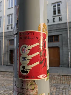 Street sticker The sticker features a striking red background with diagonal white stripes on the right, where a stylized image of hands breaking chains is depicted. On the left side, three circular icons are stacked vertically, with white arrows pointing from them towards the breaking hands. The top icon shows the 'NFF' (Norges Fotballforbund - Norwegian Football Federation) logo. The middle icon contains the text 'VAR' inside a monitor screen, representing the Video Assistant Referee system. The bottom icon displays a silhouette of a person with a dollar sign, symbolizing money or commercialization. At the top of the sticker, the text 'BESKYTT FOTBALLEN' (Protect Football) is prominently displayed. At the bottom, the phrase 'MELD DEG INN I BRANN' (Join Brann / Become a member of Brann) is written next to a logo for 'BRANN', indicating a call to action related to the SK Brann football club.
