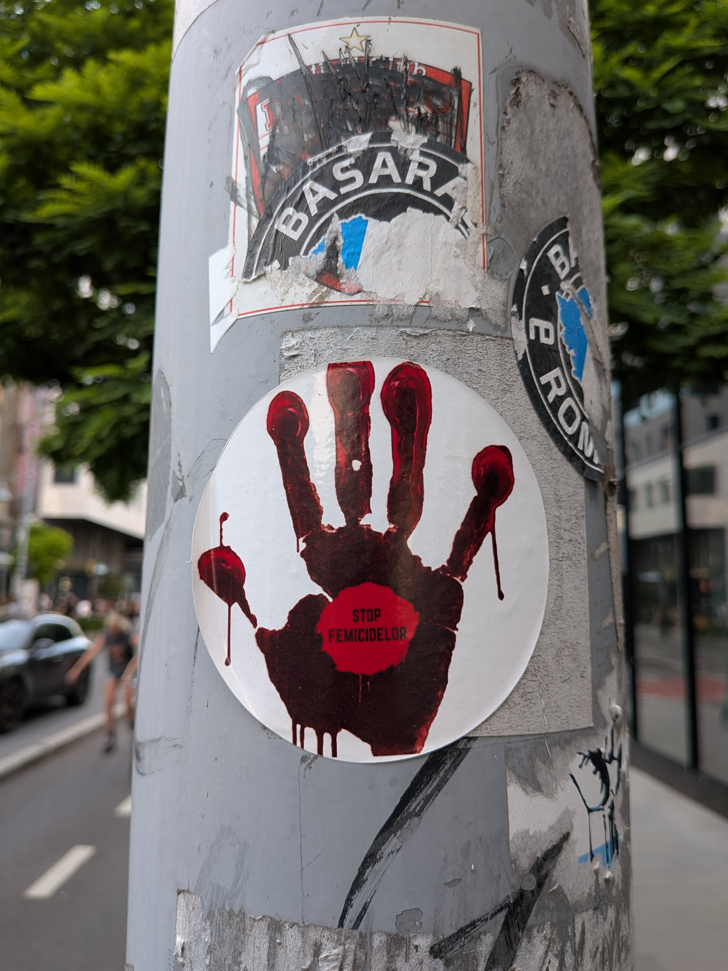 A circular white sticker depicting a dark red, dripping handprint. A bright red stamp in the center of the palm contains the text 'STOP FEMICIDELOR'.