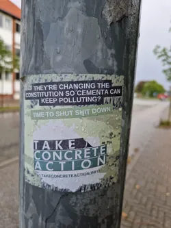 A sticker on a pole with a message about Cementa polluting and a call to action.  The sticker is wet and partially damaged. The bottom of the sticker has a website address.