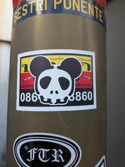 Street sticker A rectangular sticker featuring a stylized black and white panda skull over yellow, red, and black horizontal stripes. Includes Thai text, insect illustrations, and a phone number.