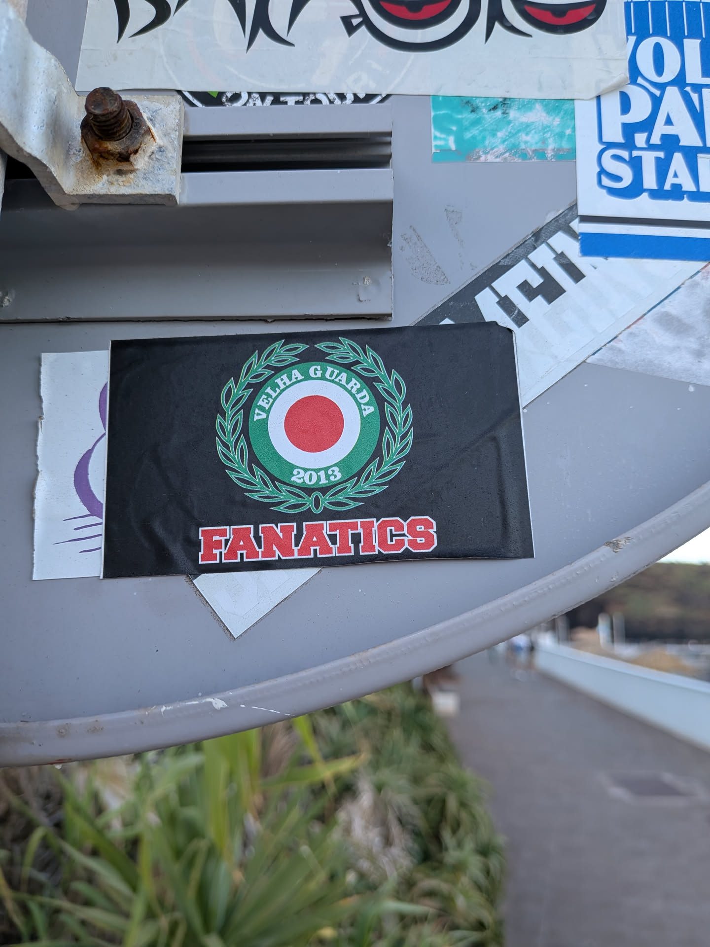 A rectangular black sticker featuring a central green, white, and red circular emblem enclosed by a green laurel wreath. The text 'VELHA GUARDA 2013' is written inside the emblem, and 'FANATICS' is printed below in red block letters with white outlines.