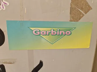 A rectangular sticker with a teal and yellow gradient background. A green triangle contains the word Garbino in pink lettering. The style is reminiscent of 90s design.