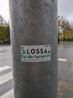 Street sticker The sticker is rectangular with a white background and a thin green border. On the left side, there is a green logo resembling an abstract building or interconnected squares. To the right of the logo, the text 'LOSSA.SE' is prominently displayed in black and green. Below this, in green text, is 'Byt din hyresrätt'. At the very bottom, in smaller grey text, it reads 'ENDAST BOSTADSBYTE I PROVA GRATIS'. In the top right corner, there is text '50 kr/år' and a small orange circular logo with a white symbol inside.