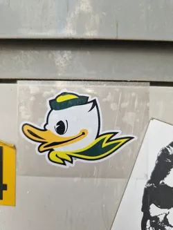 A vinyl sticker featuring the Oregon Ducks mascot, a cartoon duck wearing a yellow and green cap. The sticker is affixed to a gray surface.