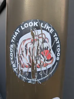 Street sticker A circular sticker on a metallic pole, heavily scratched and worn. It depicts a roaring tiger head in a traditional tattoo style with red and black details, bordered by text.