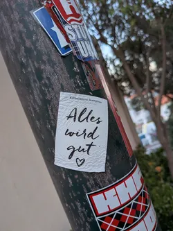 Street sticker A rectangular white sticker with a textured paper finish. It displays the small printed text 'Kaffeerösterei Deathpresso' at the top, followed by the handwritten cursive phrase 'Alles wird gut' and a small heart in black ink.