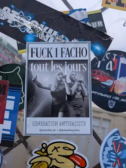 Street sticker The central sticker is a rectangular poster-style sticker with a white border. The top of the sticker features bold, black text that reads 'FUCK 1 FACHO'. Below this, in a slightly smaller, stylized font, it says 'tout les jours'. The middle section of the sticker displays a black and white photograph of a woman singing into a microphone with her arm raised, and a man behind her also holding a microphone. The bottom of the sticker has the text 'GENERATION ANTIRACISTE' in a serif font, followed by two Instagram handles: '@generation_jul' and '@jeuneprincesselena', separated by an 'x'. The sticker appears to be printed on paper and is adhered to a surface, surrounded by other torn and overlapping stickers.