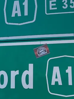 Street sticker A small, rectangular sticker featuring the official logo of FC Bayern München. The sticker's background consists of alternating dark red and red horizontal stripes. The club's circular emblem is centered on this striped background, rendered in white, blue, and red. The logo prominently displays 'F.C. BAYERN' in an outer ring and 'München' below the stylized Bavarian flag pattern in the center.