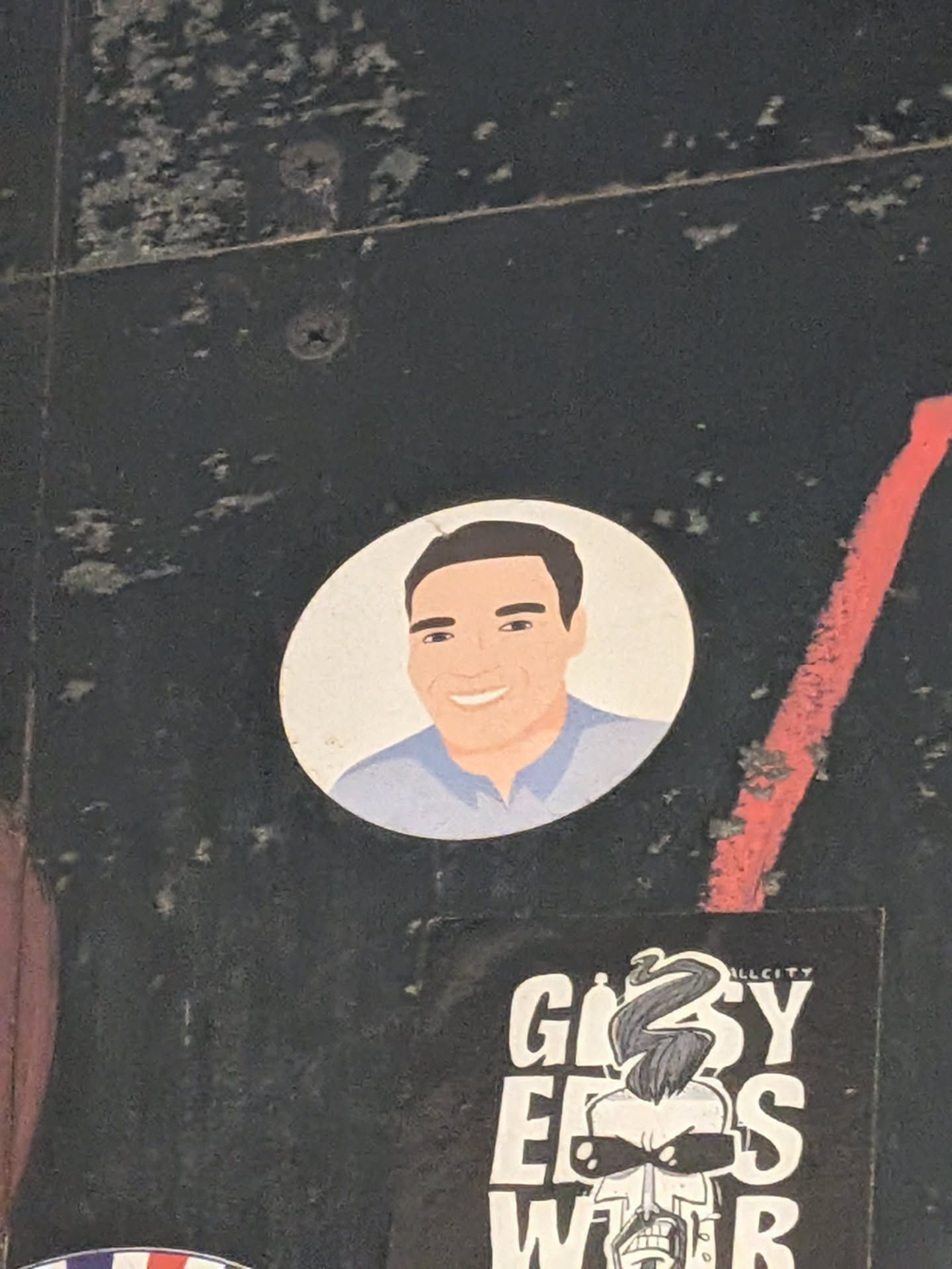 A round white sticker featuring a minimalist vector illustration of a smiling man with short dark hair and a light blue shirt.