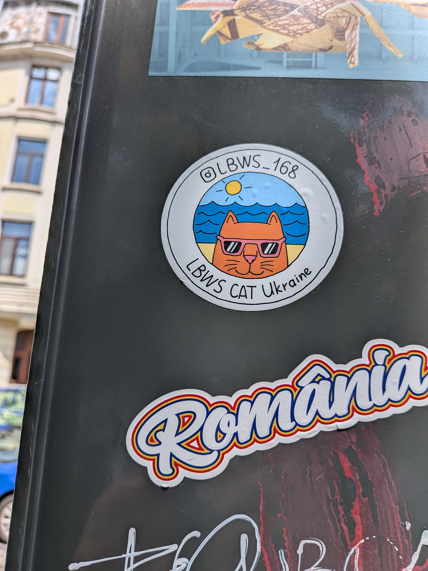 A round sticker showing an orange cartoon cat in pink sunglasses on a beach under a sunny sky. It features a white border with text and an Instagram handle.