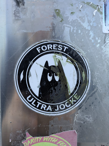 The sticker is round with a white background and a black border. The words "FOREST" and "ULTRA JOCKE" are written around the edge in black letters. Inside the circle, there is an illustration of a black mountain with eyes.