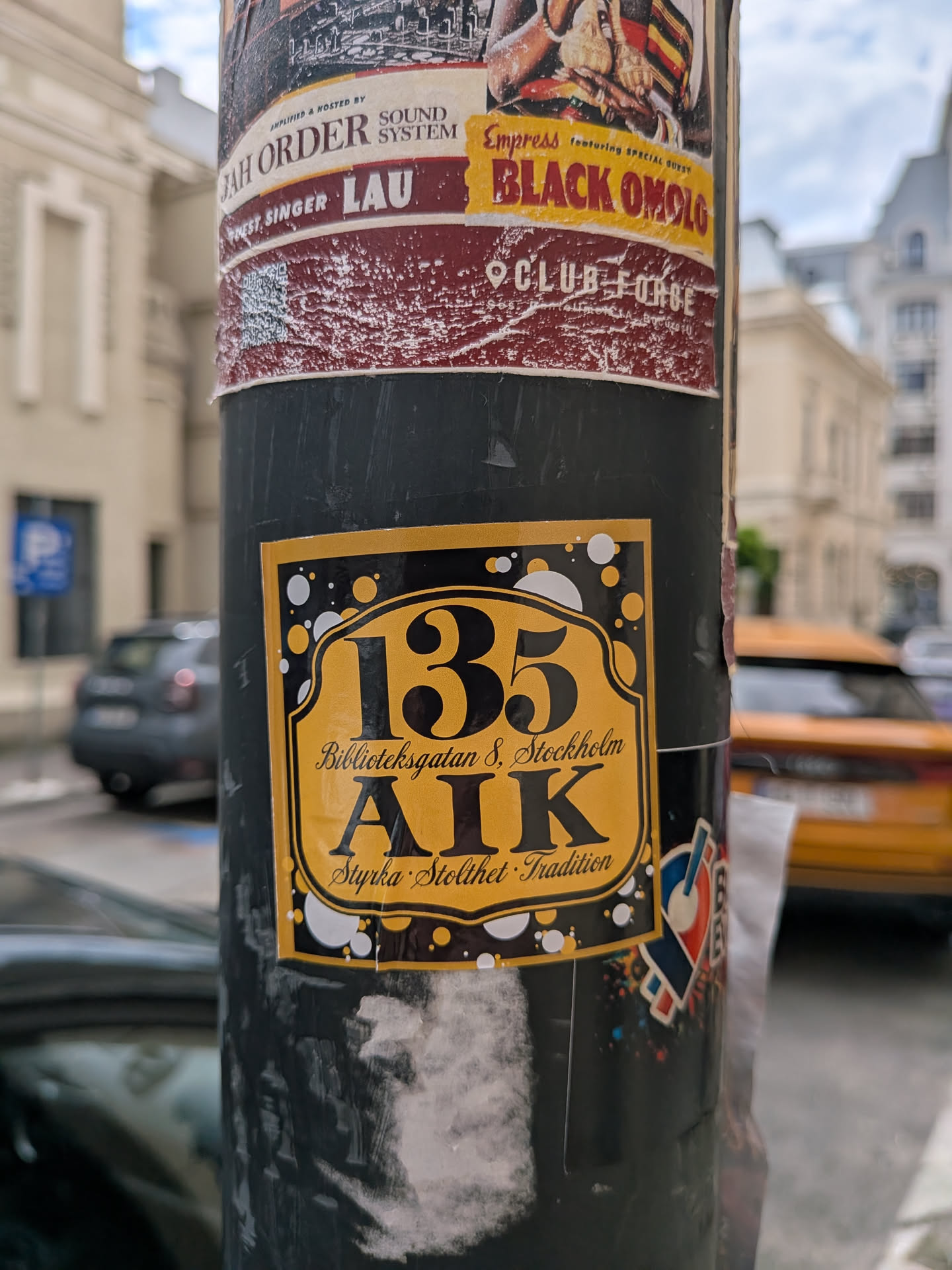 Rectangular sticker featuring a gold shield on a black, bubble-patterned background. Displays the number '135', 'Biblioteksgatan 8, Stockholm', 'AIK', and the motto 'Styrka · Stolthet · Tradition'.