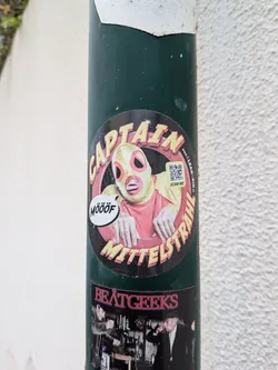 Street sticker A round sticker with a black background showing a character in a yellow and pink mask. The words 'CAPTAIN MITTELSTRAHL' are written in a bold, stylized yellow font. Includes a speech bubble saying 'MÖÖÖF' and a QR code pointing to cleanurin.de.