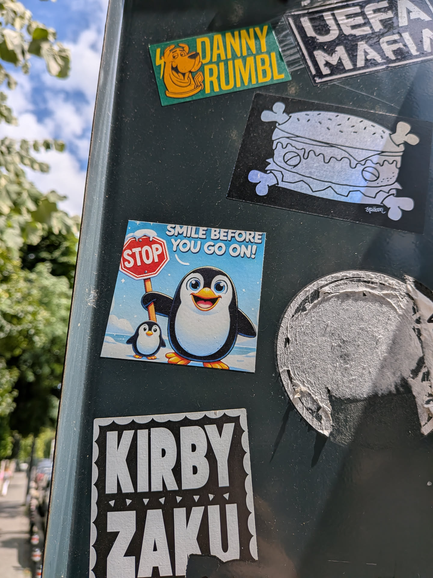 A square sticker depicting a cheerful cartoon penguin holding a snowy 'STOP' sign next to a smaller penguin. The background is a light blue sky, and the text 'SMILE BEFORE YOU GO ON!' is written at the top.