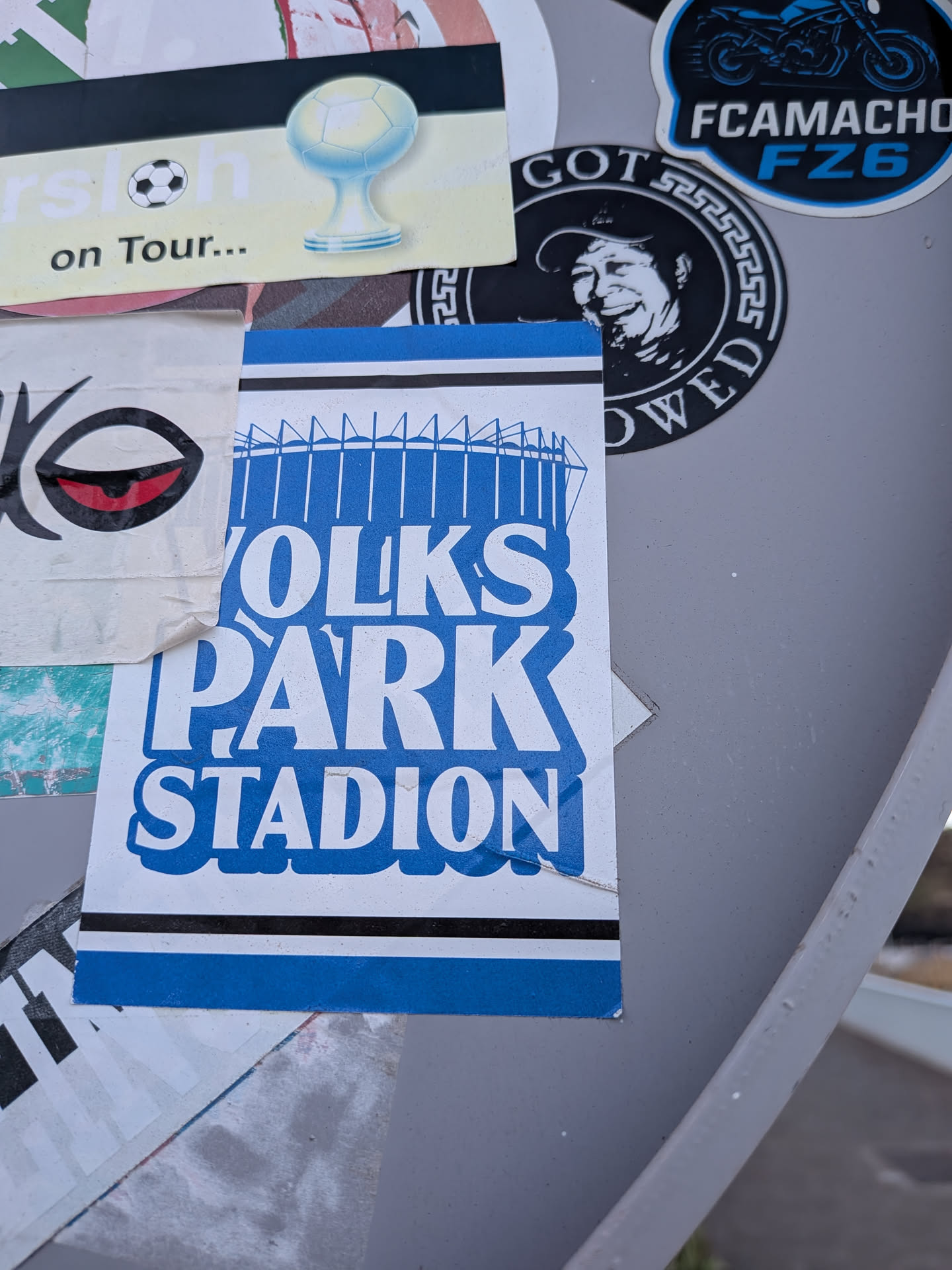 A rectangular sticker with blue and black stripes at the top and bottom. The center features the text 'VOLKSPARK STADION' in bold white letters on a blue background, topped with a blue line drawing of the stadium's roof structure.