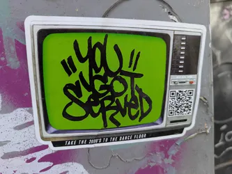 Street sticker The sticker is designed to look like an old-fashioned television set with a green screen. The text "YOU GOT SERVED" is written in bold black graffiti on the screen. Below the screen, the text reads "TAKE THE 2000'S TO THE DANCE FLOOR". There's a QR code labeled "SCAN ME" on the right side of the TV.