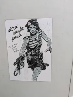 Street sticker This sticker features a drawing of a woman wearing a striped shirt and a beret with a St. Pauli logo on it. She is holding a gun and has other equipment strapped to her. The text on the sticker says "Ultra Sankt Pauli" and "it's not just boys fun!".