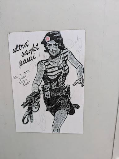 This sticker features a drawing of a woman wearing a striped shirt and a beret with a St. Pauli logo on it. She is holding a gun and has other equipment strapped to her. The text on the sticker says "Ultra Sankt Pauli" and "it's not just boys fun!".