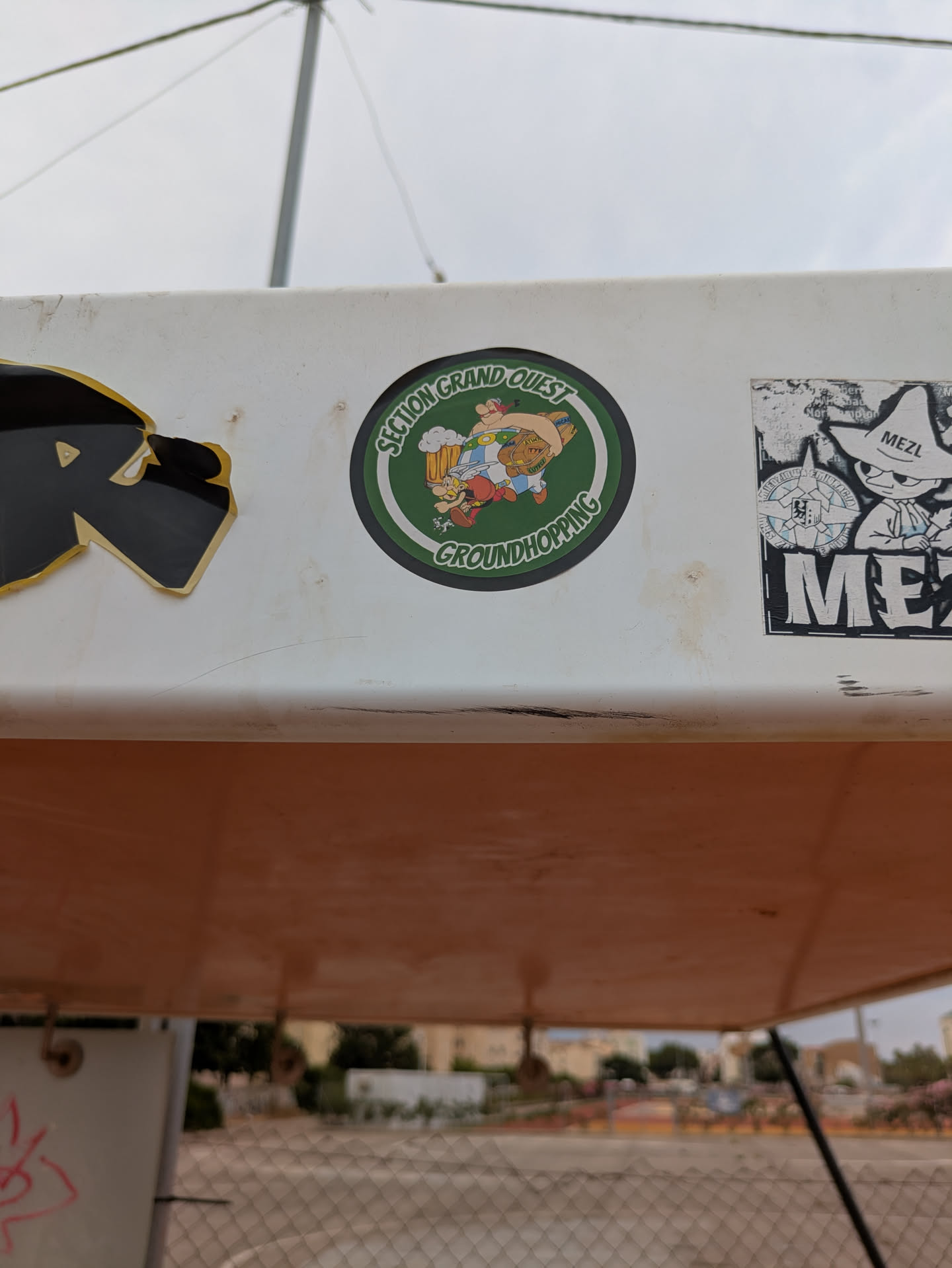 Street sticker This round sticker shows two characters inspired by the French comic book series Asterix and Obelix. The characters are caricatures with humorous features. One of them looks like Asterix drinking beer while the other is a larger character looking like Obelix holding a large barrel. The text "Section Grand Ouest GROUNDHOPPING" is featured around the image.