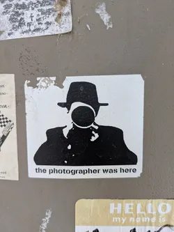Street sticker This is a black and white sticker with a silhouette of a person in a hat, holding a camera to their face. The text at the bottom says "the photographer was here."