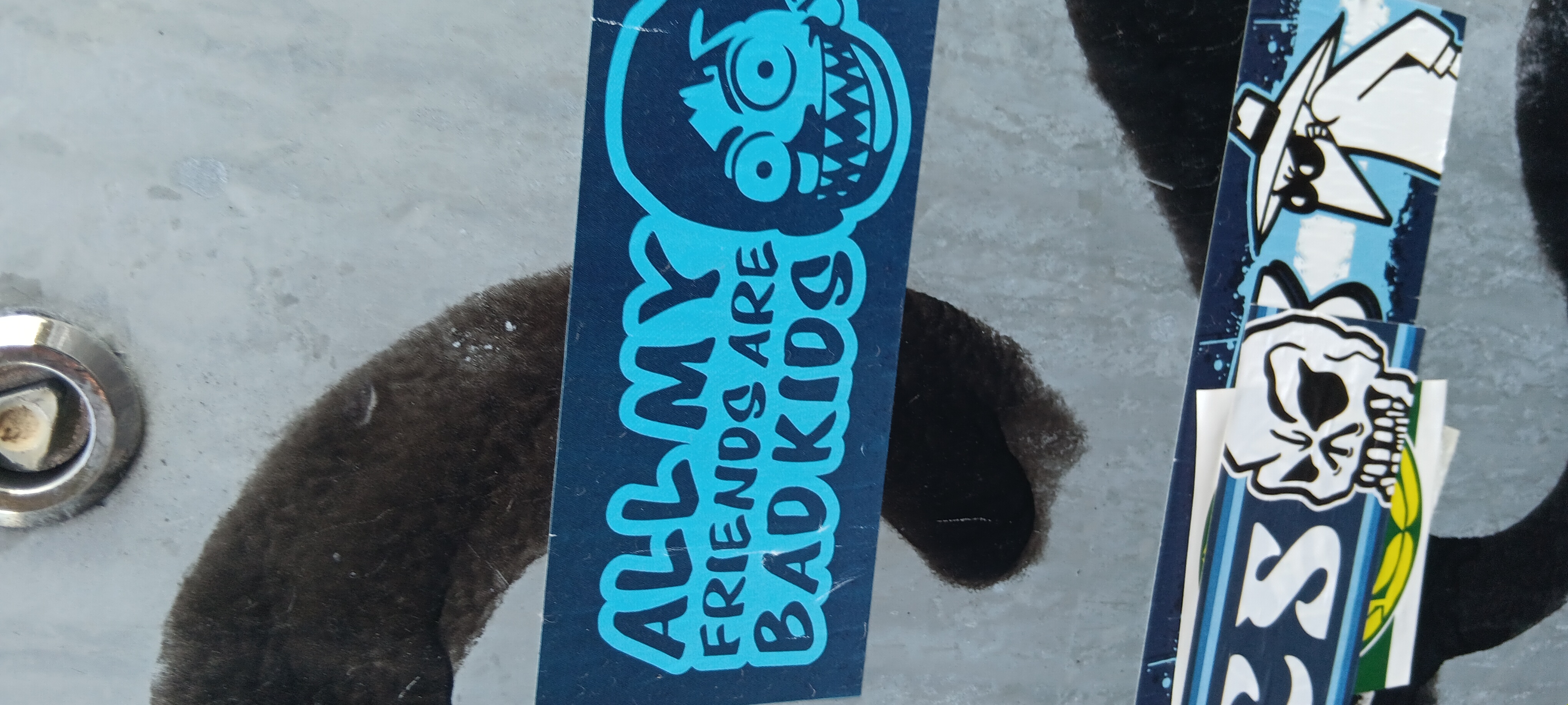 A blue sticker with a cartoonish monster face at the top and the text "All My Friends Are Bad Kids" written vertically down the sticker. There are other stickers to the right, including one with a skull.