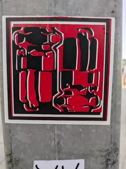 This sticker features an abstract design in red, black, and white. It has a thick black border on a white background. The shapes within the sticker are geometric and somewhat resemble stylized figures or objects. It is affixed to a metal pole.