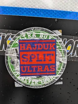 Street sticker A sticker featuring the text 'Hajduk Split Ultras' in a layered design. The main text is set against a red and purple background, inside a circular green design.  The sticker shows some signs of wear and tear.