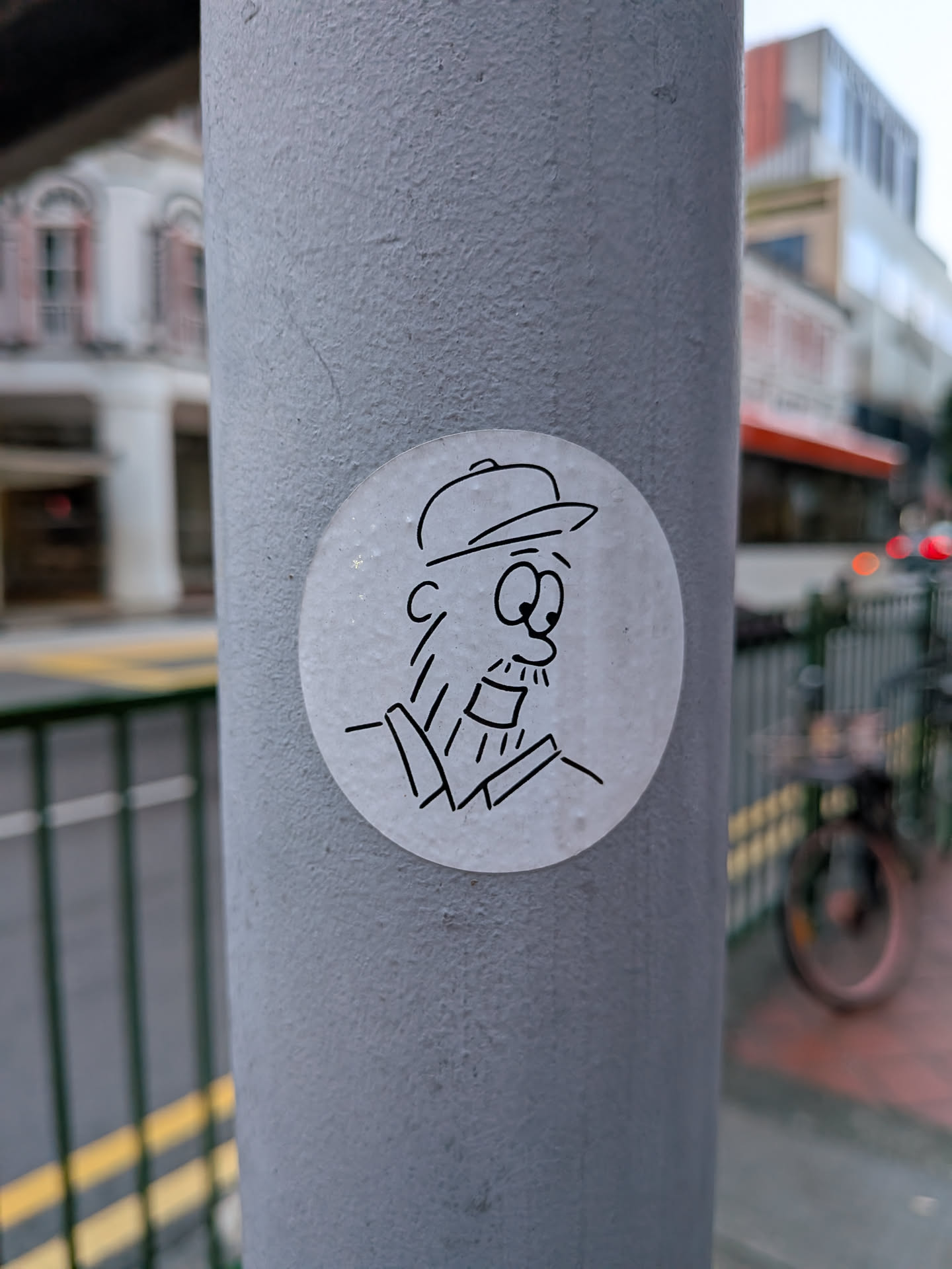 A circular white sticker featuring a simple black line drawing of a bearded man wearing a baseball cap and a collared shirt.